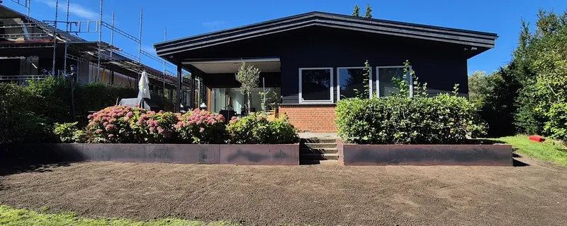 Have under anlæg foran moderne villa med cortenstålkanter og klargjort jord til beplantning
