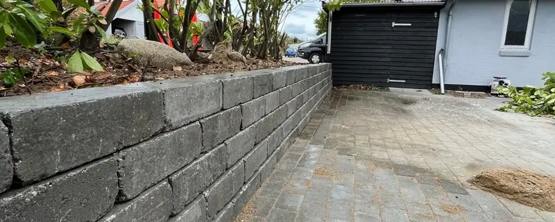 Støttemur i grå betonblokke langs nylagt indkørsel i belægningssten