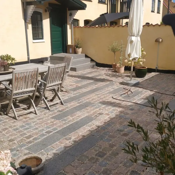Gårdterrasse med belægning i chaussésten og fliser, havemøbler og parasol