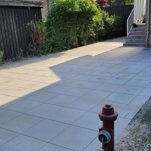 Belægning i store grå fliser langs hus med sort træhegn