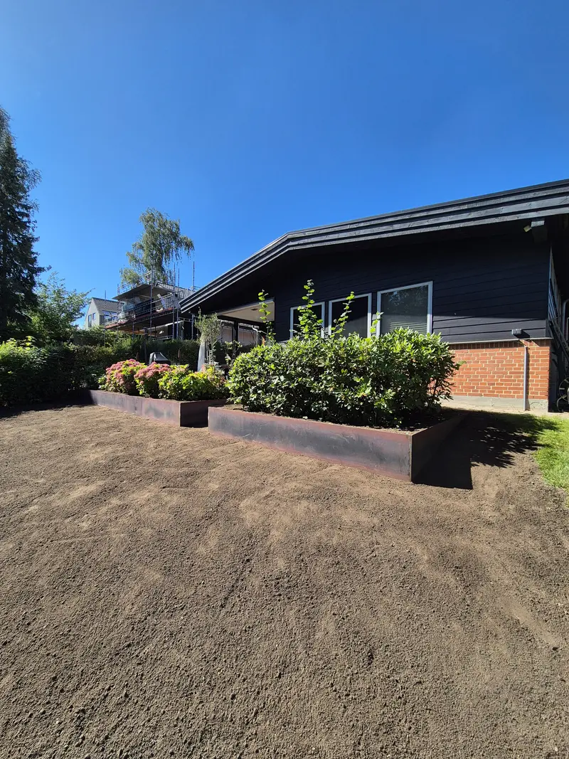 Cortenstålkant om bed med beplantning langs hus og afrettet muld