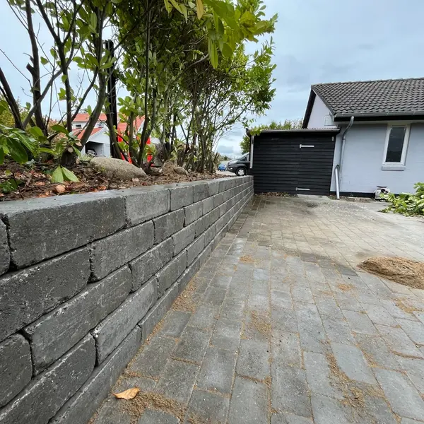 Støttemur i grå betonblokke langs indkørsel med belægning