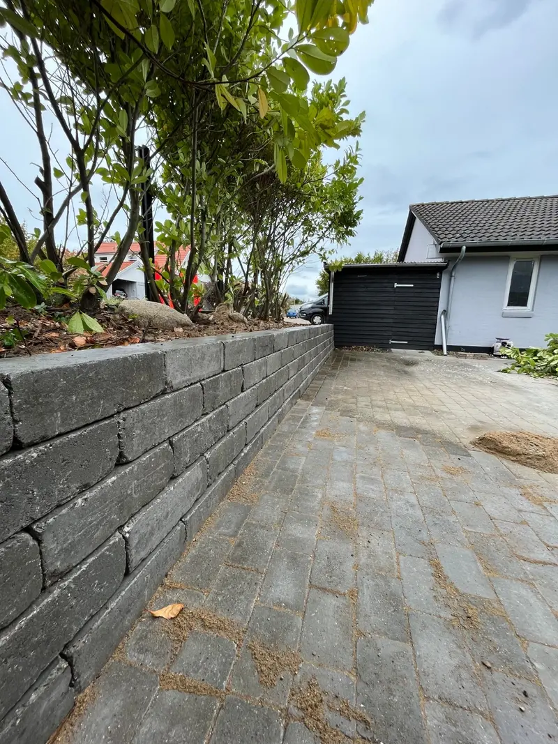 Støttemur i grå betonblokke langs indkørsel med belægning