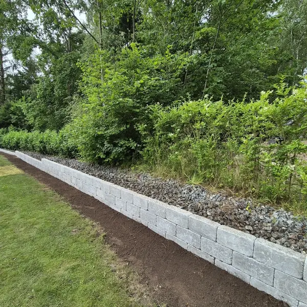 Lav støttemur i betonblokke langs græsplæne med grus og beplantning