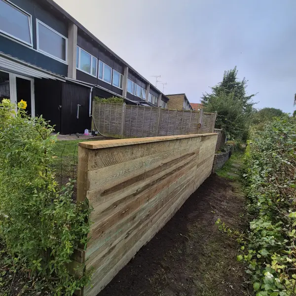 Lang støttemur i vandrette træplanker langs sti ved rækkehuse